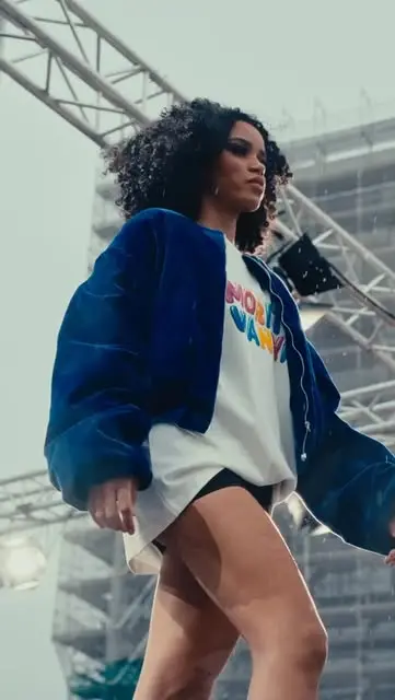 Model on an outdoor scaffold runway wearing a blue velvet bomber jacket over a printed tee