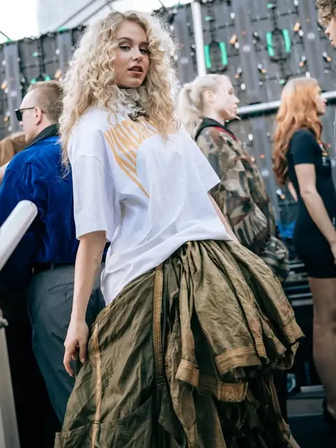 Blonde model backstage wearing a white printed tee and a voluminous olive parachute-silk skirt