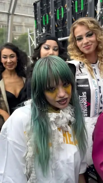 Backstage: model with green hair and yellow eye make-up laughing with the crew