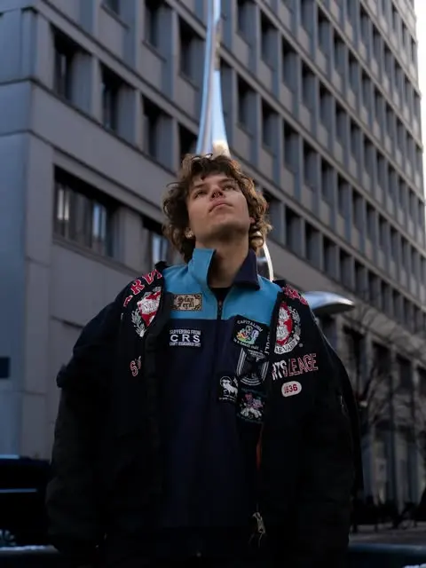 Lennart Wobig in a patched bomber jacket looking up between high-rises