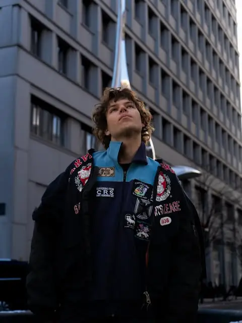 Lennart Wobig in a patched bomber jacket looking up between high-rises